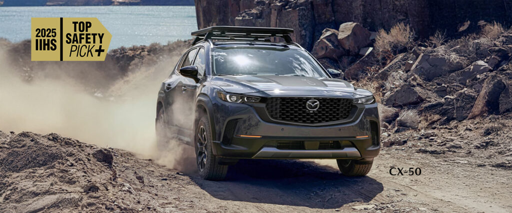 2025 Mazda CX-50 gray SUV driving off-road by a lakeside, certified IIHS Top Safety Pick+ for outstanding safety